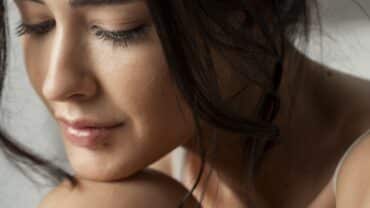 Imagem fechada no rosto de uma mulher. Ela está com o queixo apoiado em um dos joelhos e olhando para baixo, como se ela estivesse na dúvida se pode usar hidrante corporal no rosto.