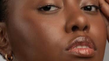 Imagem fechada no rosto de uma mulher preta. Ela está com a mão sobre a testa, como se estivesse em fazendo reflexões no ritual de cuidados com a pele.