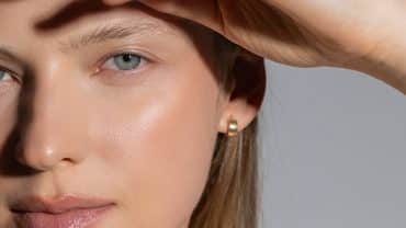 Imagem fechada no rosto de uma mulher. Ela tem a pele e os olhos claros e está recebendo luz natural no rosto. Sua pele está radiante com os cuidados pós-sol.